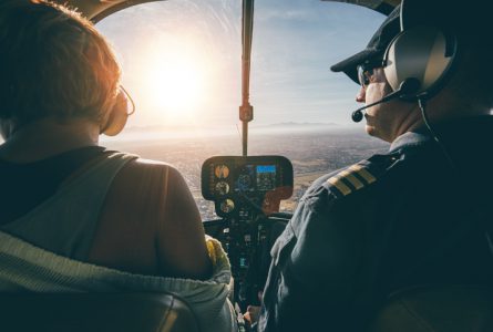 Rear view of male and female pilots flying a helicopter on sunny day. Man flying a helicopter with his copilot looking outside the aircraft.