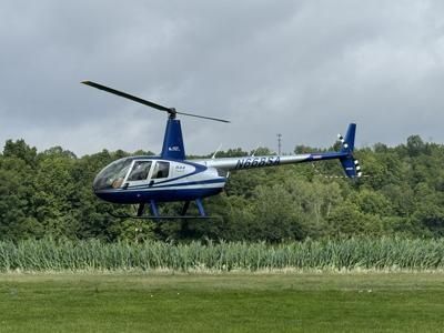 Blåvit helikopter svävar lågt över ett gräsfält under molnig himmel