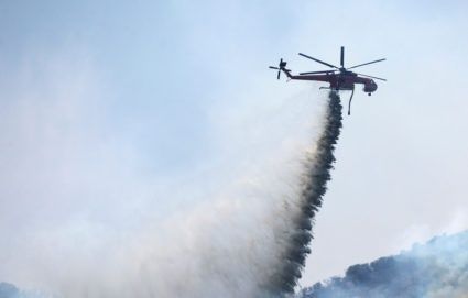 Helikopter släpper en tät vattenstråle över ett rökfyllt skogsområde