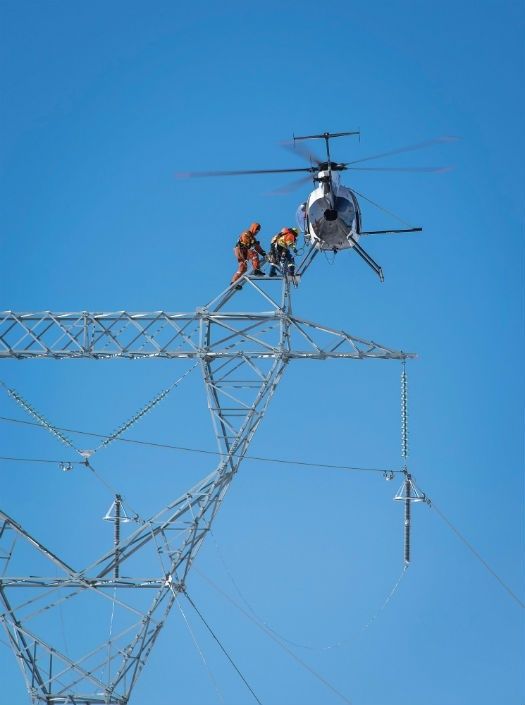 Helikopter hovrar nära tekniker på en högspänningsledning